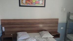 A neatly made bed with a patterned bedspread and pillows, a wooden headboard, a small bedside table with a lamp, and a framed picture on the wall. - Hotel Michel (São Paulo)