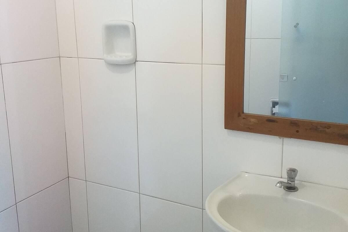 A bathroom with white tiled walls, a white sink, and a mirror with a wooden frame.