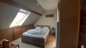 Un dormitorio con techo inclinado, cama con ropa de cama blanca, mesita de noche, lámpara y un cuadro en la pared.
