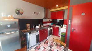 Una cocina compacta con armarios rojos, un refrigerador de acero inoxidable, un microondas y una cafetera.