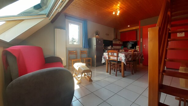 Una habitación acogedora con techo inclinado, una mesa de comedor con sillas, un sofá rojo y un taburete pequeño.