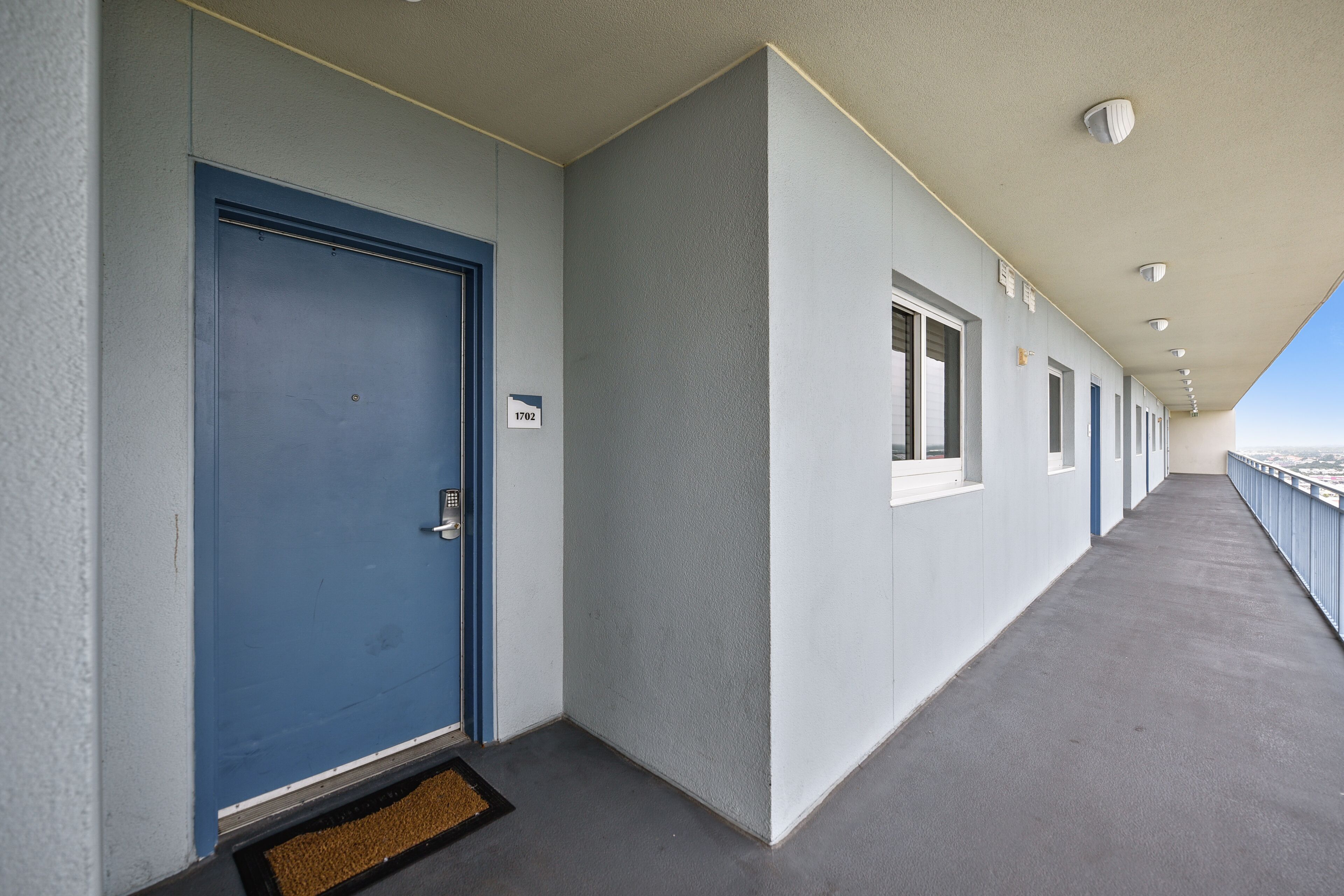 A corridor with a blue door, numbered 1702, leading to a room.