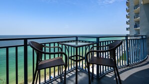 Un balcon avec des fauteuils en osier et une table, d’où l’on a vue sur une plage et l’océan.