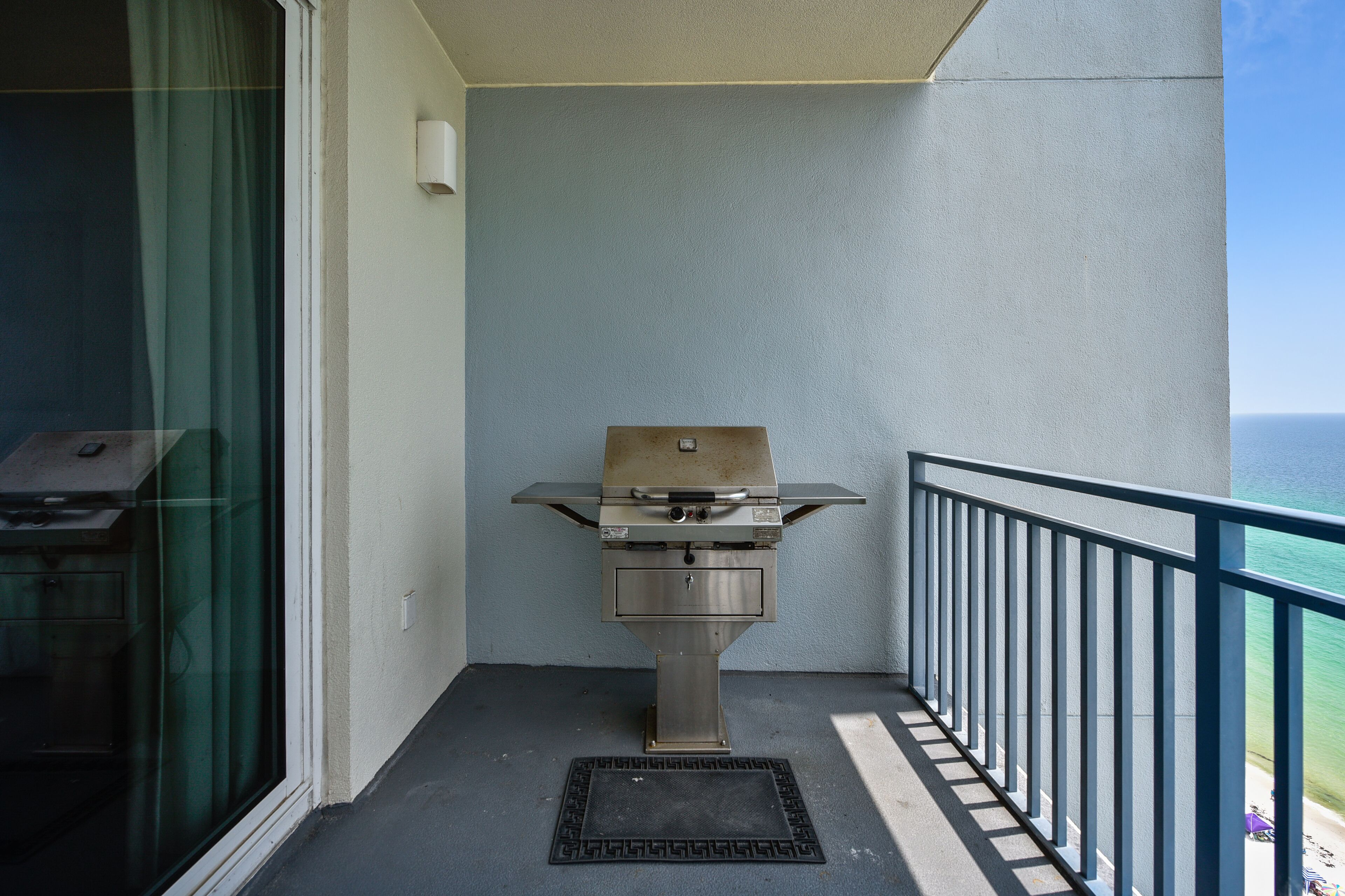 Een balkon met een barbecue, uitzicht op de oceaan en een hekwerk.