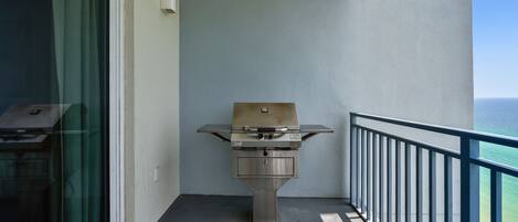 Een balkon met een barbecue, uitzicht op de oceaan en een hekwerk.