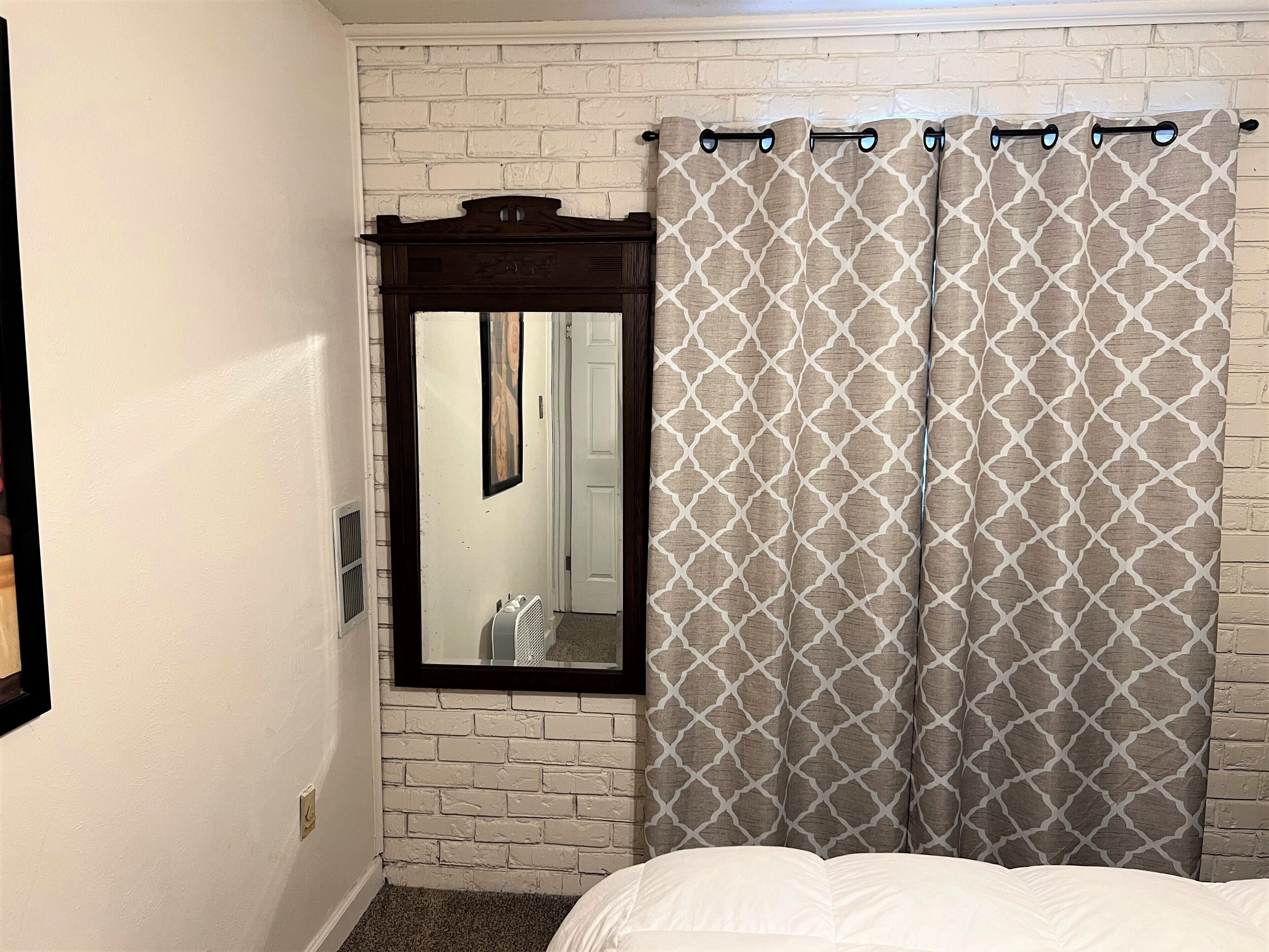 A bedroom with a white brick wall, a large mirror, and a bed with white bedding.