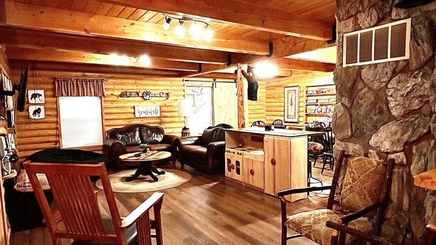 A cozy log cabin interior with a wooden ceiling, stone wall, and a fireplace. There are wooden chairs, a sofa, and a dining table. - MAMA BEAR CABIN -RUSTIC LOG  Cabin Retreat -  Boat Parking - All Size Groups (Garden City)