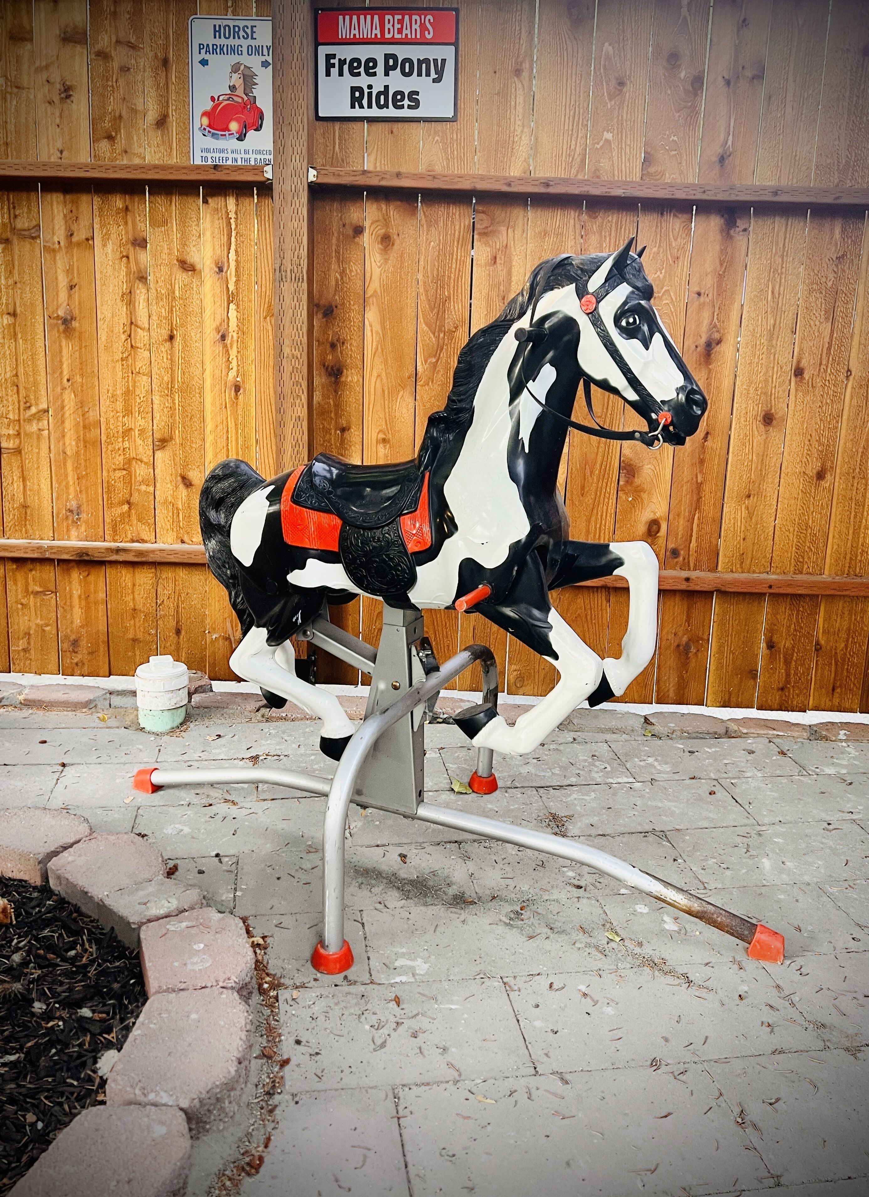 A decorative horse sculpture mounted on a metal stand with a wooden fence in the background.