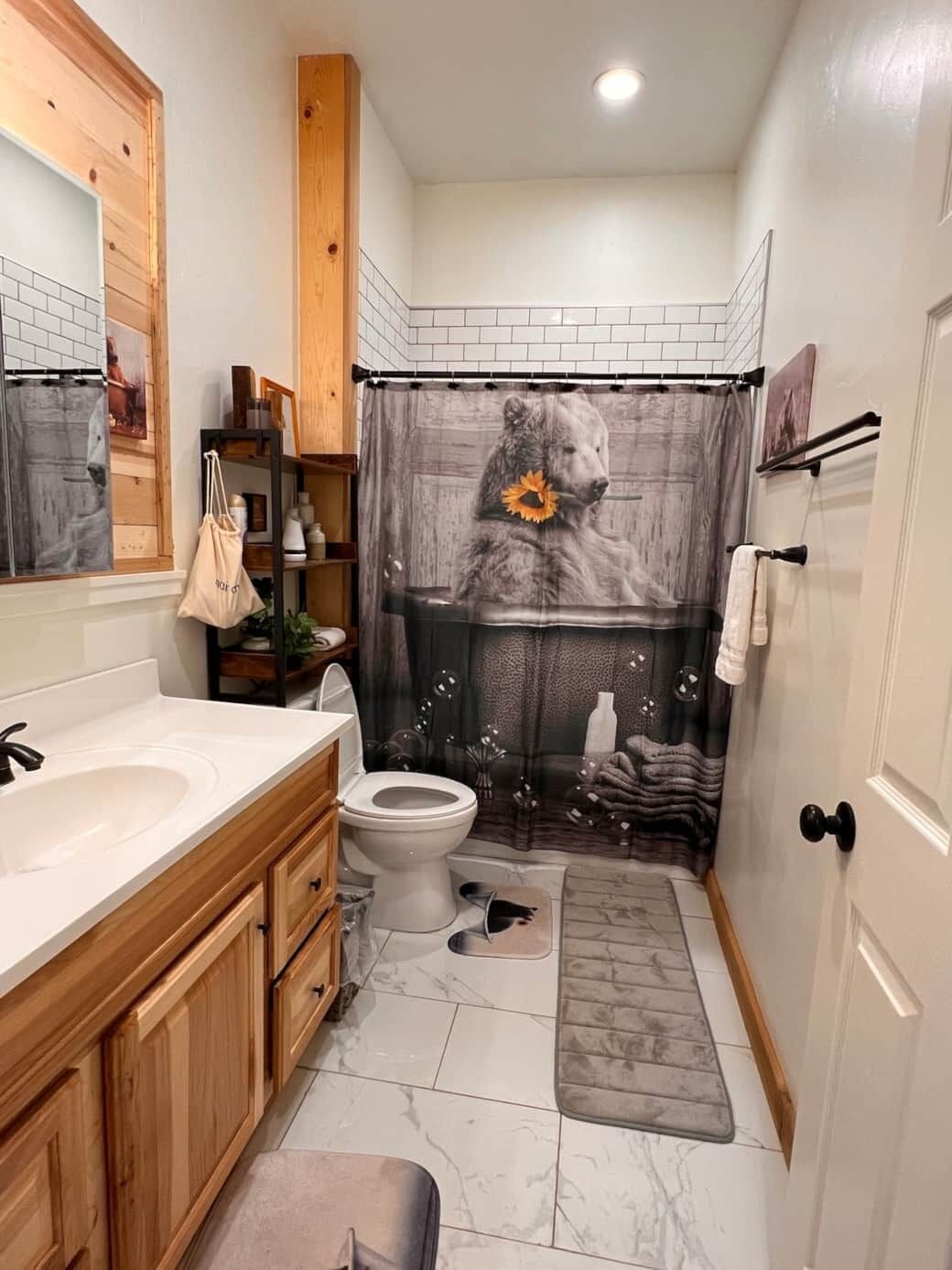 A bathroom with a wooden vanity, a toilet, a shower curtain with a bear design, and a marble floor.