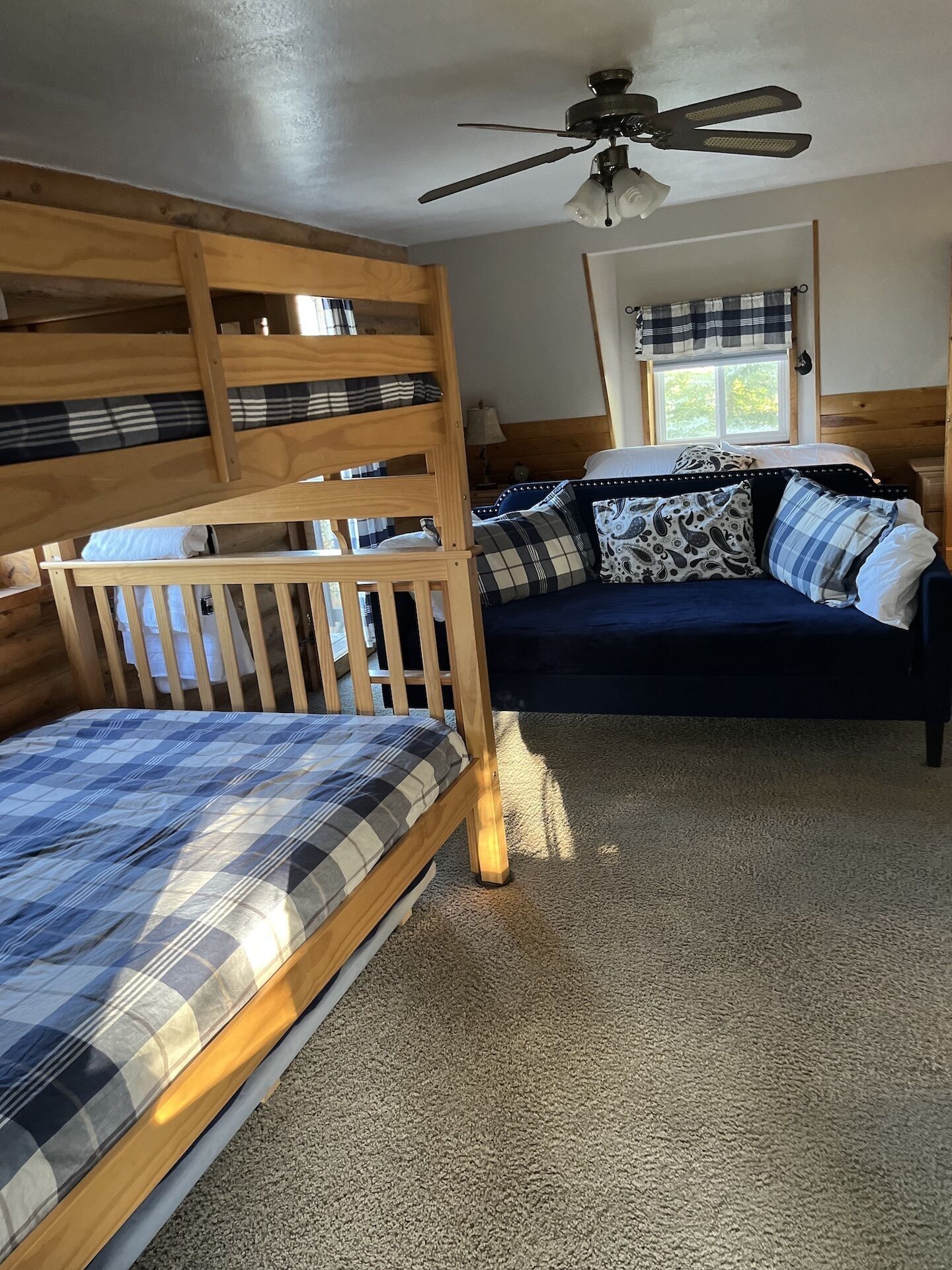 A room with a bunk bed, a sofa bed, a ceiling fan, and a window with curtains.