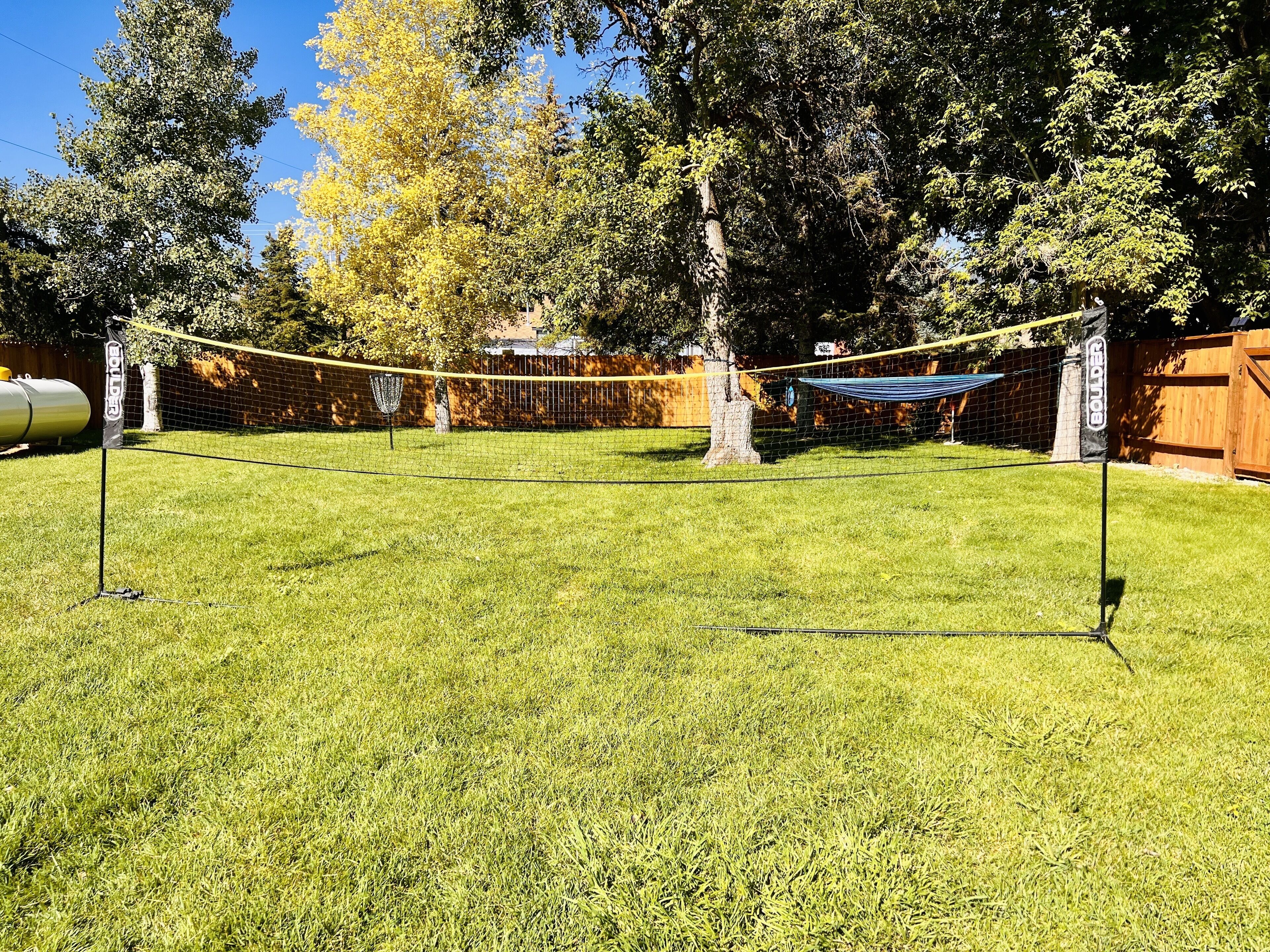 A backyard with a volleyball net, a hammock, and a trampoline.