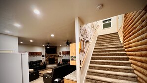 A spacious living area with a fireplace, a kitchen with a refrigerator, and a wooden staircase. - MAMA BEAR CABIN -RUSTIC LOG  Cabin Retreat -  Boat Parking - All Size Groups (Garden City)