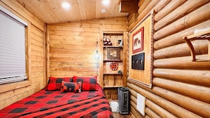 A log cabin bedroom with a bed, a small table, and a shelf with items. - MAMA BEAR CABIN -RUSTIC LOG  Cabin Retreat -  Boat Parking - All Size Groups (Garden City)