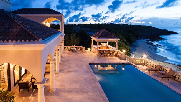 Un área de piscina exterior lujosa con un pabellón, vistas al océano y un patio bien iluminado.