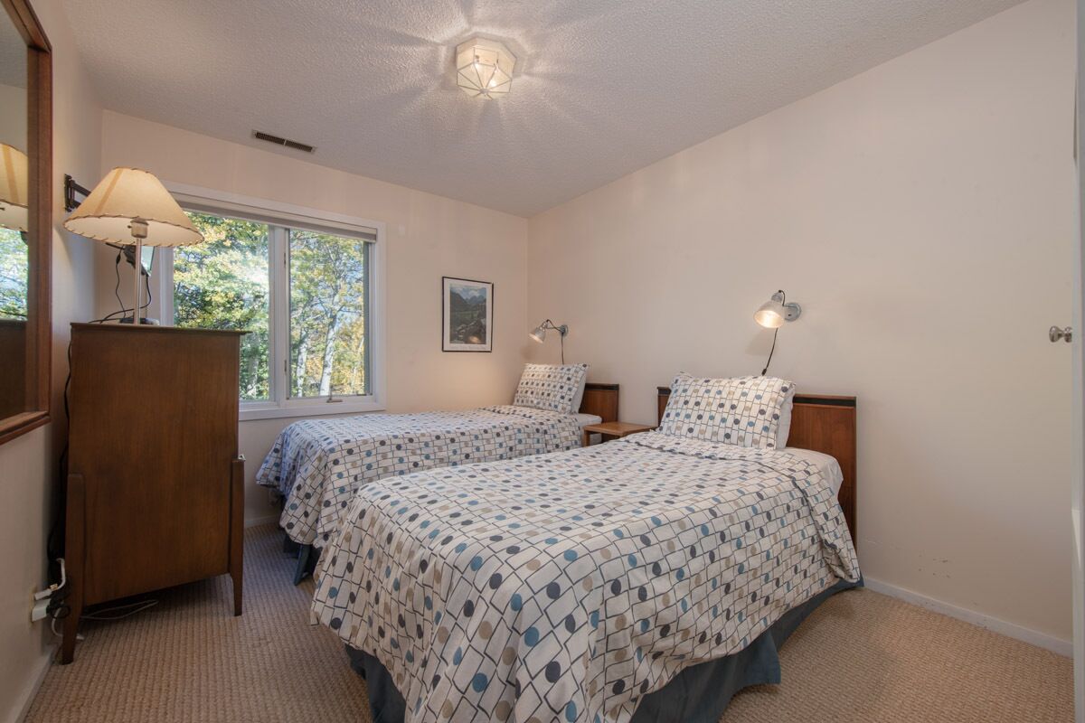 A bedroom with two beds, a dresser, a desk, and a window with a view of trees.