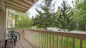 A wooden deck with a railing, two green chairs, and a view of a forested area with trees and a road.