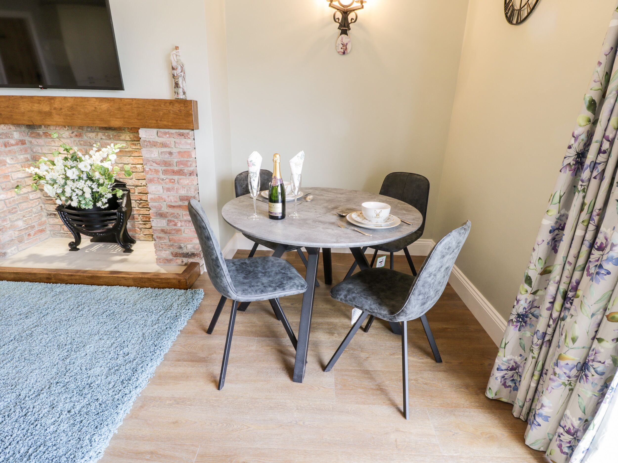 A dining area with a round table, four chairs, a bottle of champagne, and a bowl.