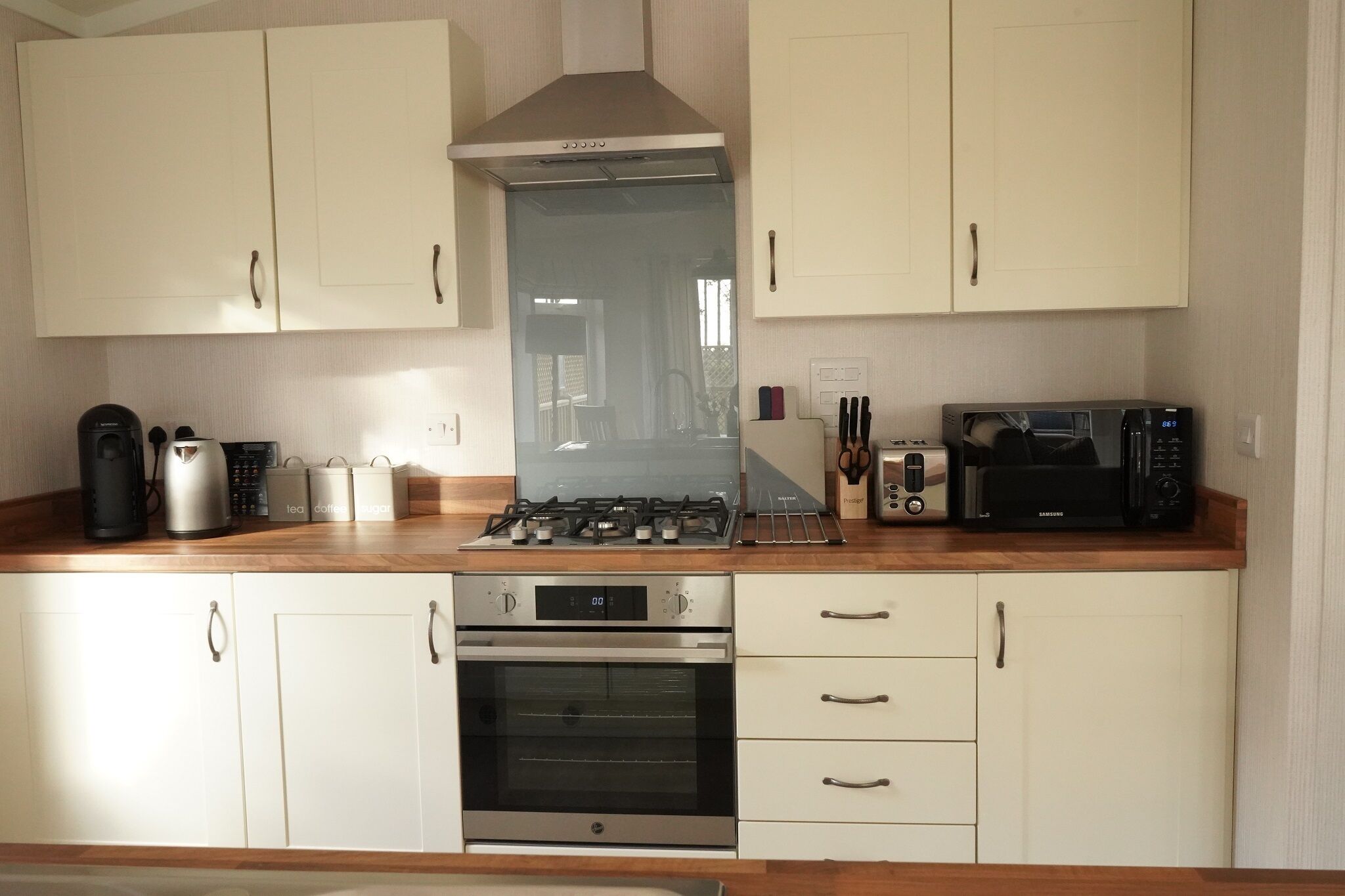 A modern kitchen with white cabinets, stainless steel appliances including a stove, oven, and microwave, and a coffee maker.
