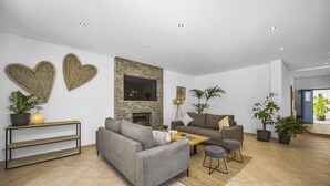 A modern living room with a grey sofa, a coffee table, and two armchairs. There are two large heart-shaped wall decorations and a fireplace. - Villa Falesia Blue by Villa Plus (Olhos de Água)