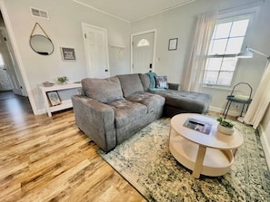 A living room with a grey sectional sofa, a round coffee table, a patterned rug, and a white console table with a plant.