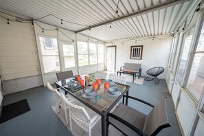 A covered patio with a table set for dining, chairs, and a chair with a backrest.