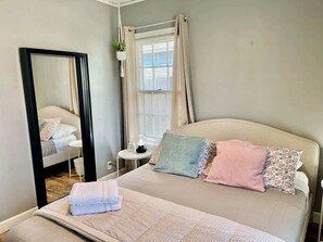A bedroom with a bed, a bedside table, a mirror, and a window with curtains.