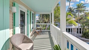 A covered porch with a wicker chair, a small table, and a view of a pool and palm trees. - ~Reel Paradise~Beautiful private townhouse in a small gated community. (Key West)