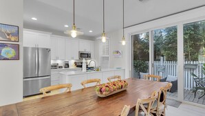A modern kitchen with white cabinets, stainless steel appliances, and a wooden dining table with chairs. - ~Reel Paradise~Beautiful private townhouse in a small gated community. (Key West)