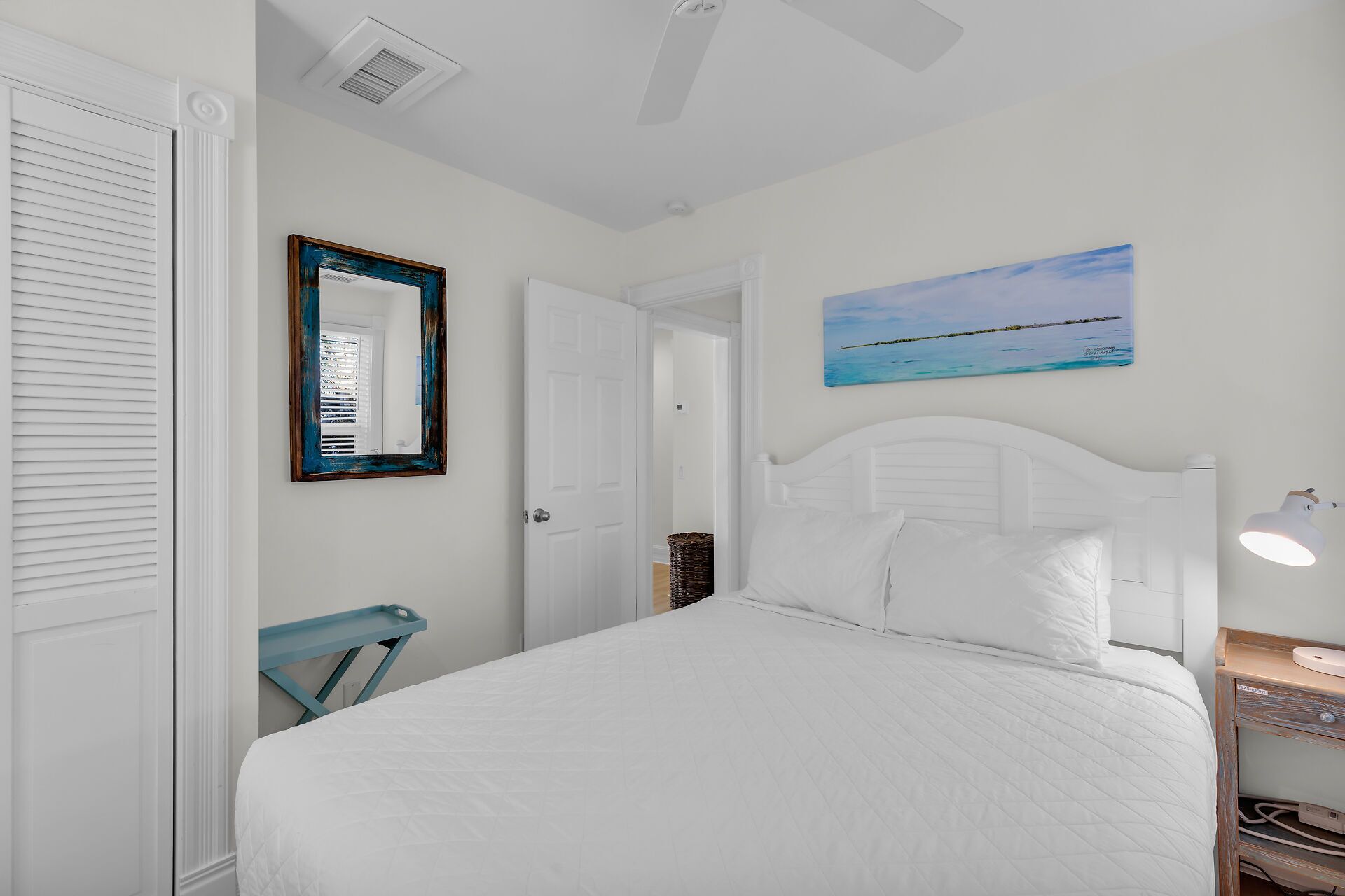 Una camera da letto con un letto, una porta bianca, uno specchio, un quadro e un comodino con una lampada.