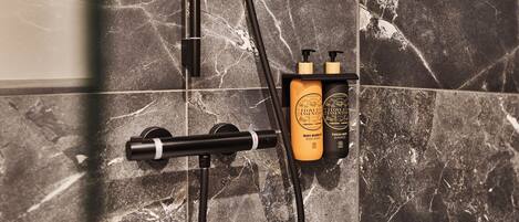 A bathroom with a black marble wall, a showerhead, and two bottles of body wash and shampoo on a shelf.