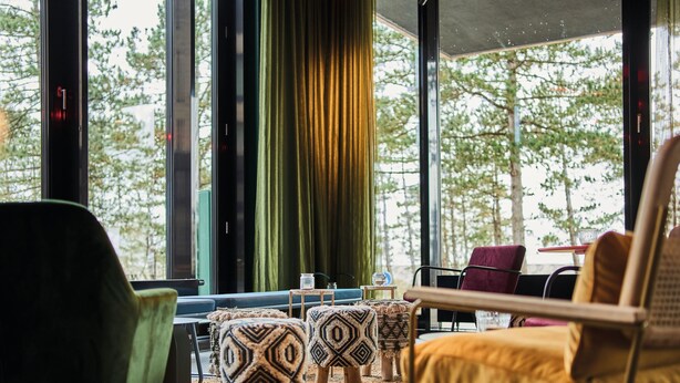 Un interior moderno con una zona de estar que incluye una silla verde, un sillón amarillo y otomanas estampadas.