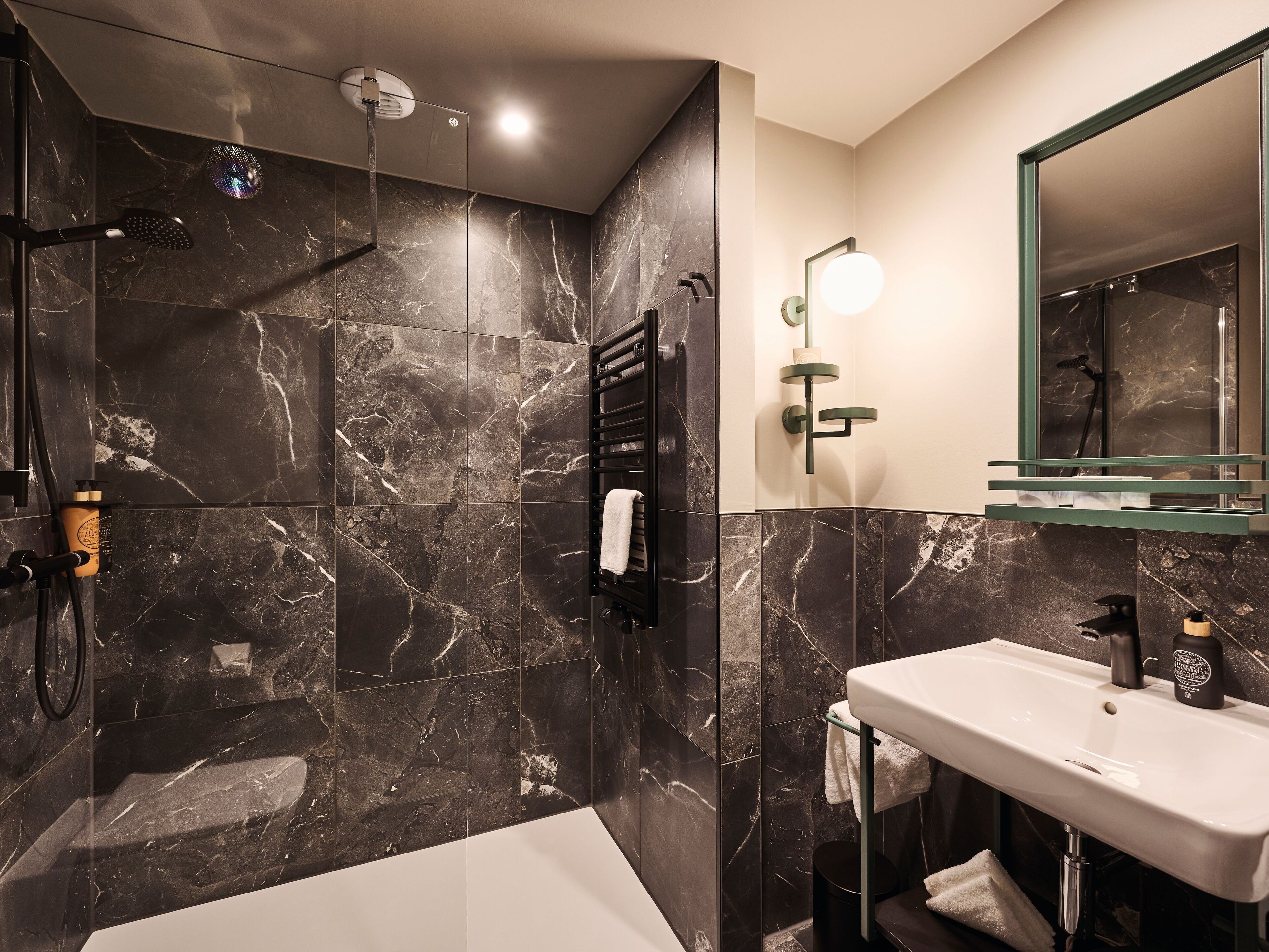 A modern bathroom with a marble shower, a white sink, and a large mirror.