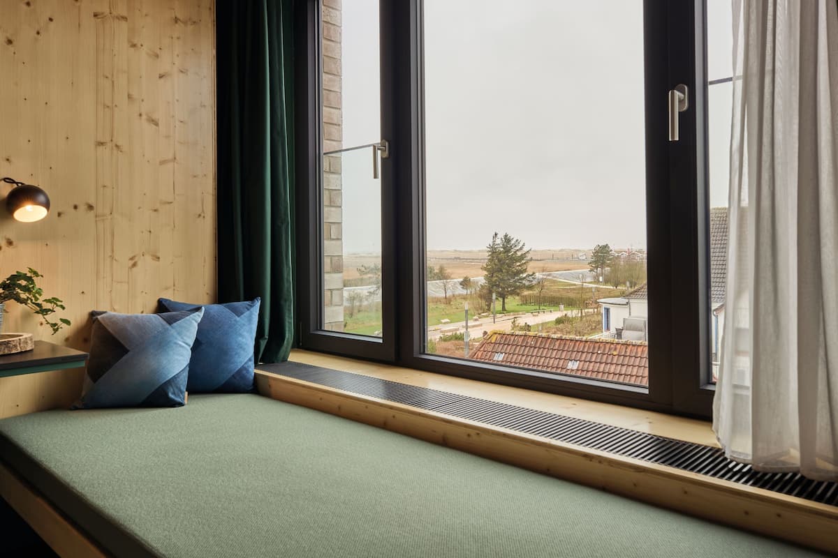Una habitación con un ventanal grande, una cama con ropa de cama verde y vistas a un paisaje urbano.