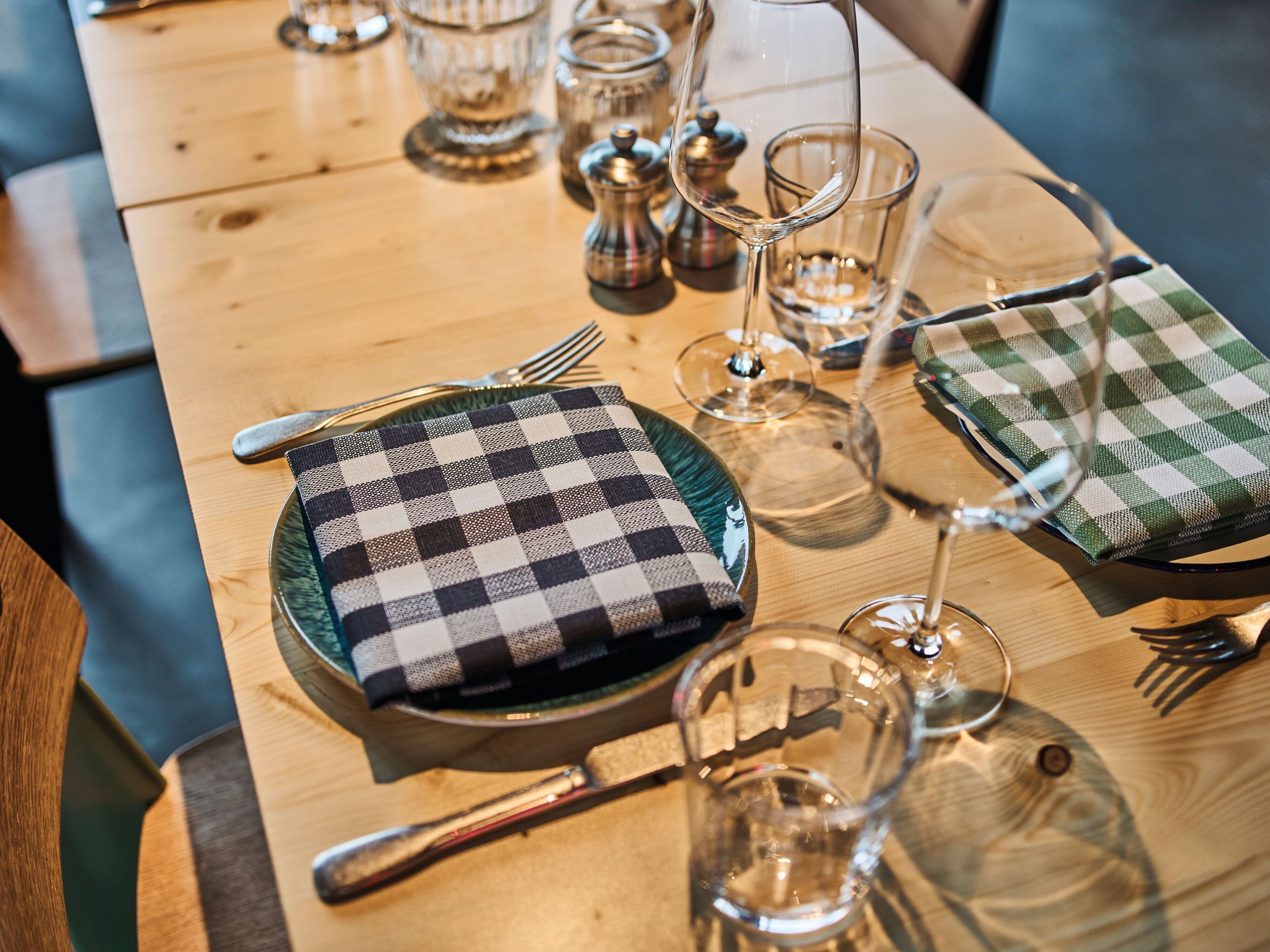 A dining table set with plates, cutlery, glasses, and a checkered napkin.