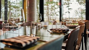 Mesa de restaurante dispuesta con copas de vino y cubiertos, con vista a árboles a través de amplios ventanales.