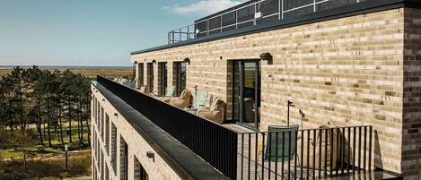 A modern building with a balcony, large windows, and a view of the beach.