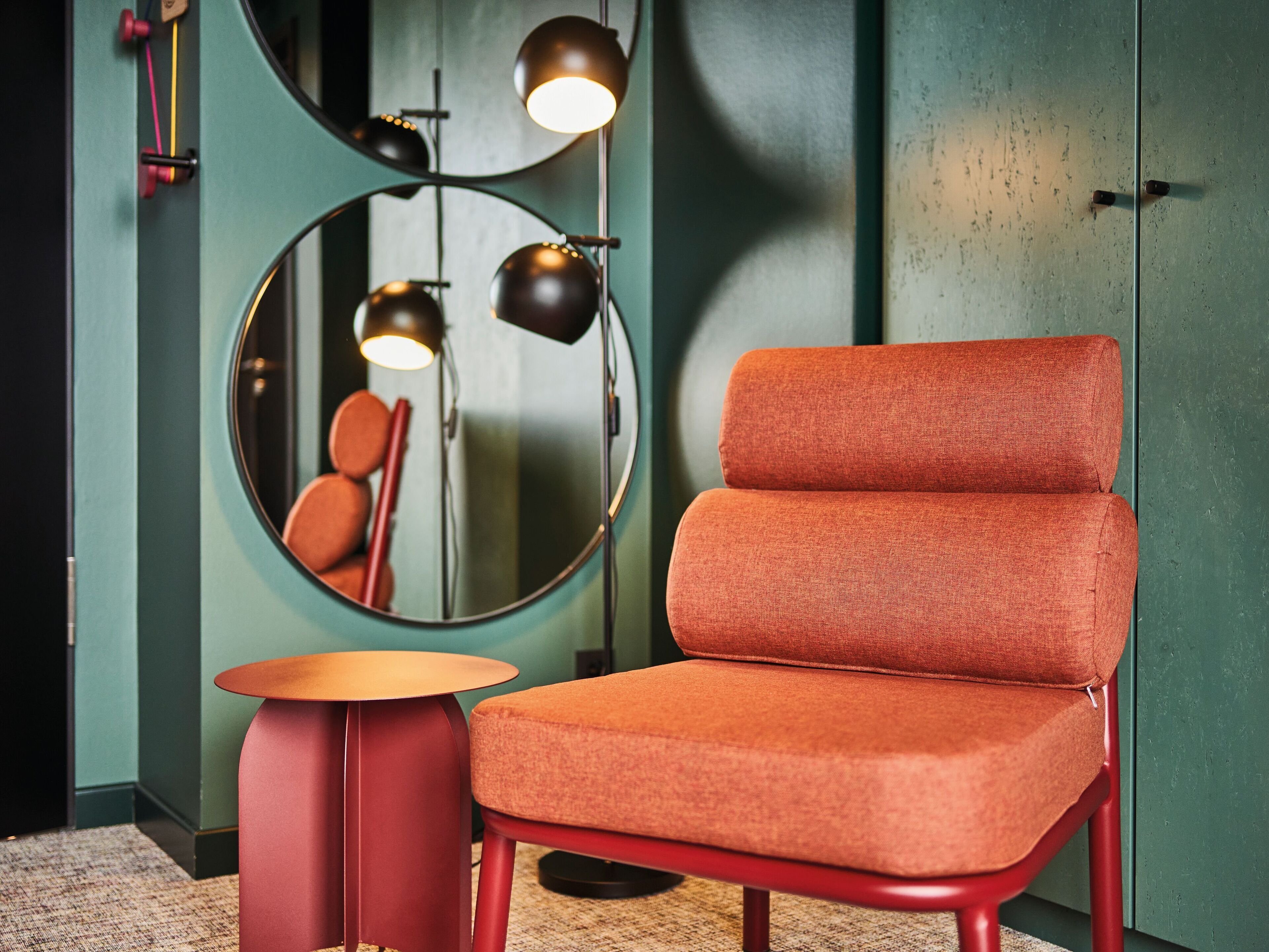 A modern room with a round mirror, a red chair, and a small round table.