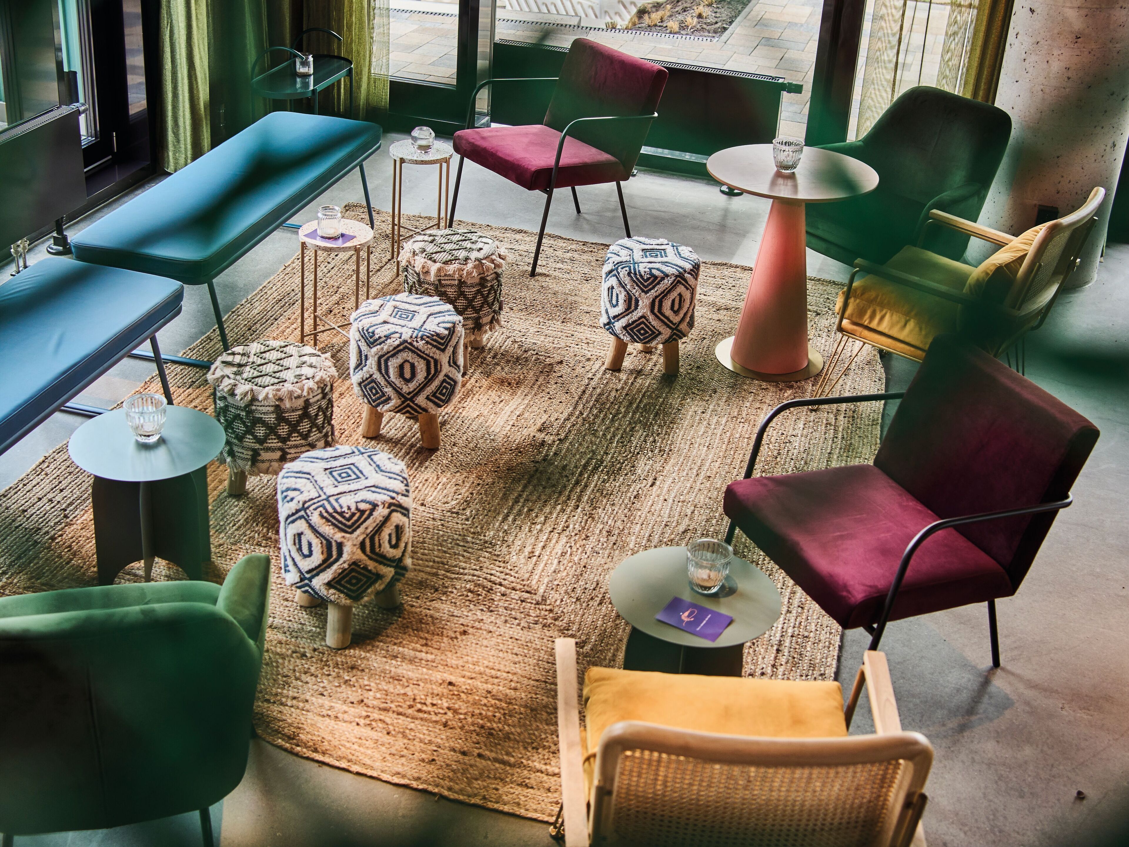 A modern interior with a mix of seating options including a bench, chairs, and ottomans. There are small tables with glassware and a rug on the floor.
