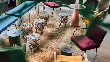 A modern interior with a mix of seating options including a bench, chairs, and ottomans. There are small tables with glassware and a rug on the floor.