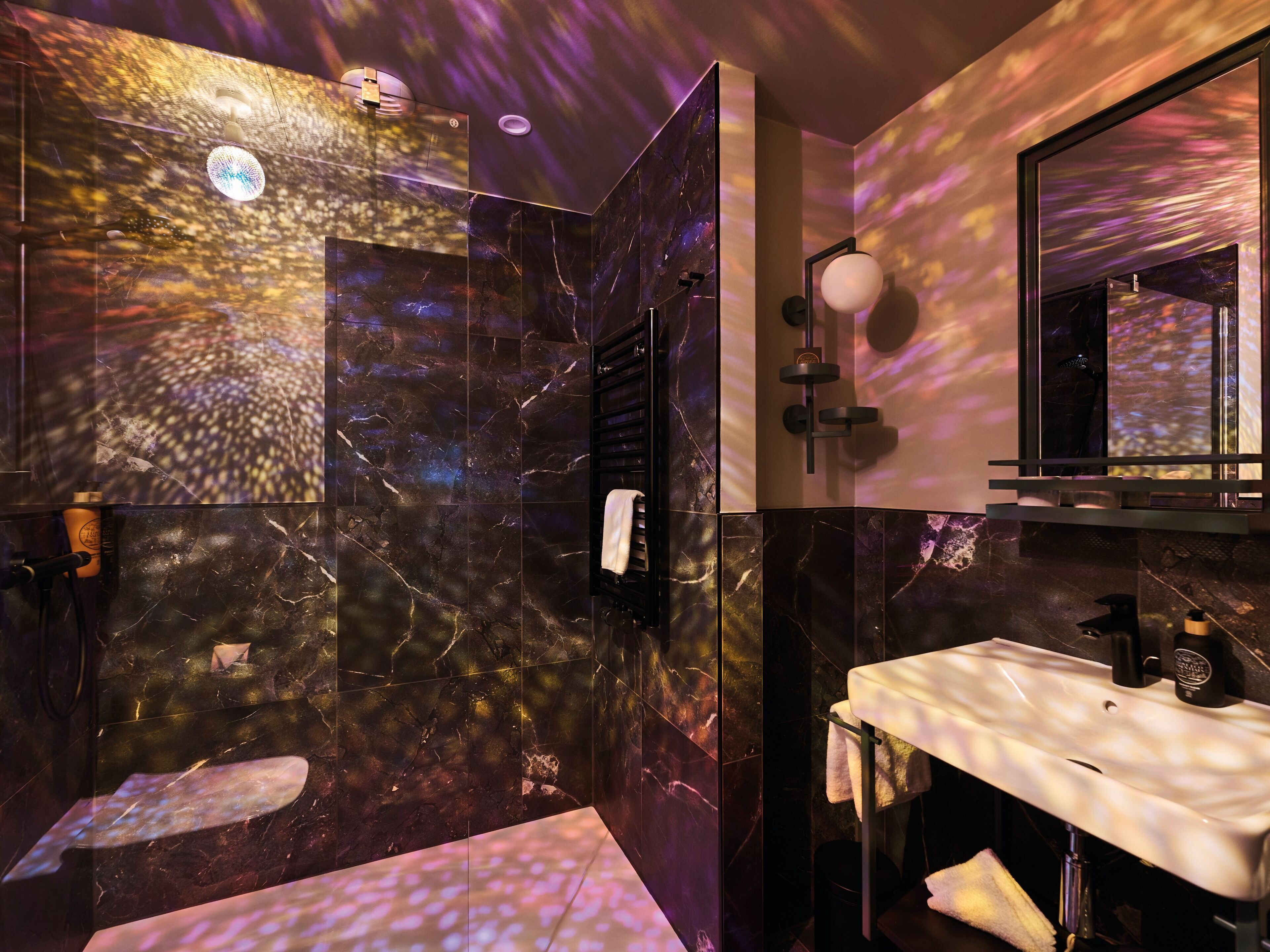 A modern bathroom with a marble wall, a white sink, and a shower area.
