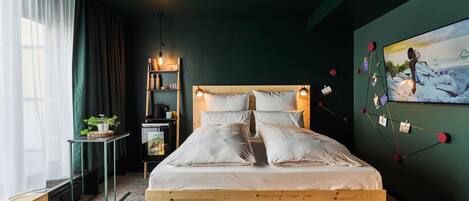 A modern bedroom with a wooden bed, a small bedside table, a shelf with books and a plant, and a wall-mounted TV displaying a scenic image.