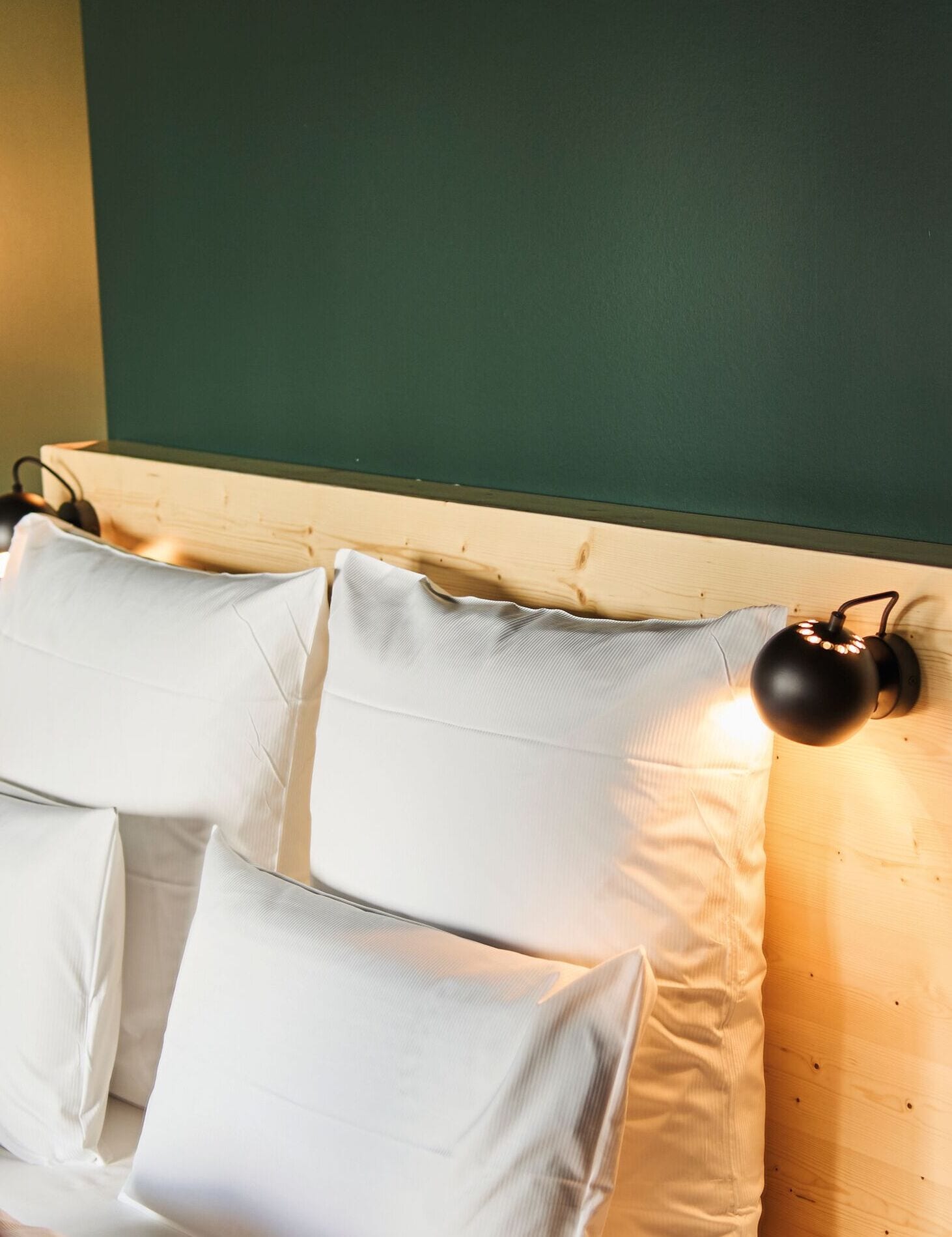 Un lit avec des oreillers blancs et une lampe noire fixée au mur.