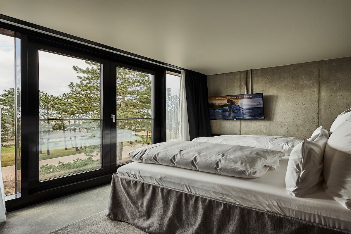Un dormitorio con un ventanal grande, una cama con ropa blanca y un cuadro en la pared.