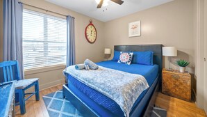 A bedroom with a bed, a ceiling fan, a clock, a bedside table with a lamp, and a window with curtains. - The Lofts of Downtown (540 N 2nd St, #105) (Clarksville)