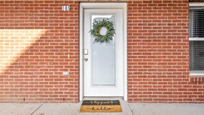 A brick building with a white door, a number '105' above it, and a doormat with 'shoppe' and 'hello' on it. - The Lofts of Downtown (540 N 2nd St, #105) (Clarksville)