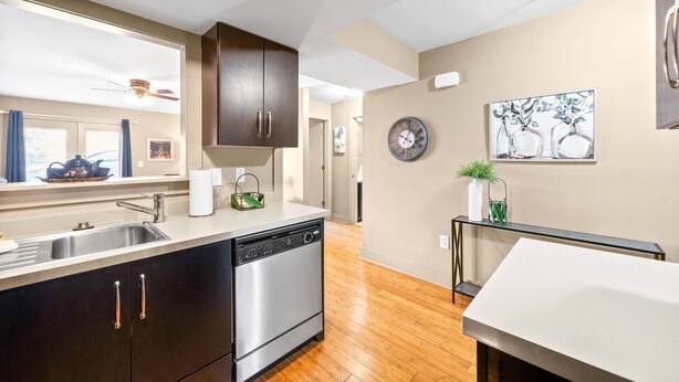 A modern kitchen with a dishwasher, dark cabinets, a window with curtains, a clock, and a painting on the wall. - The Lofts of Downtown (540 N 2nd St, #105) (Clarksville)