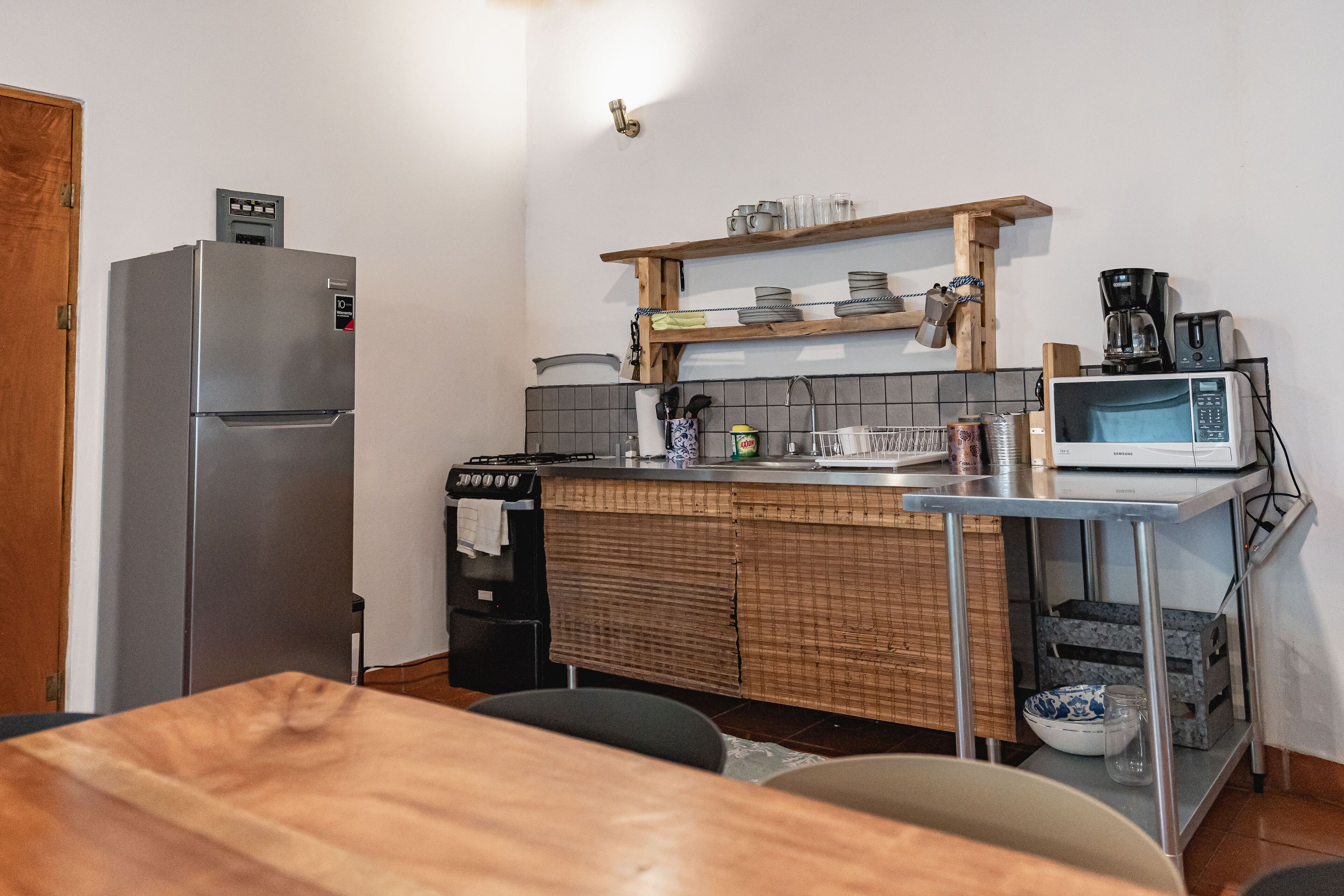 A compact kitchen with a refrigerator, microwave, stove, and wooden shelves.