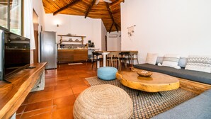 Un'accogliente zona giorno con soffitto in legno, un divano, un tavolino da caffè e una cucina sullo sfondo.