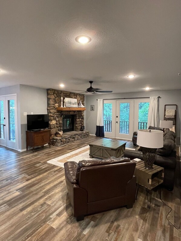 A spacious living room with a stone fireplace, a television, leather sofas, and a ceiling fan. - 2BR 2Bath Condo Tree top view located at Lake Ouachita.. (Mount Ida)