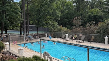 A swimming pool surrounded by a fence, with trees in the background and a few people around.